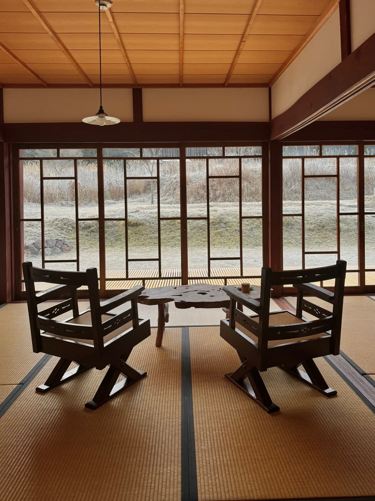 Two wooden chairs and a low table beside garden-facing windows